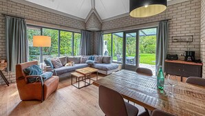 A spacious living area with a large sofa, a coffee table, and a dining table. There are large windows offering a view of the outdoors. - Nice home in Dirkshorn with WiFi (Dirkshorn)