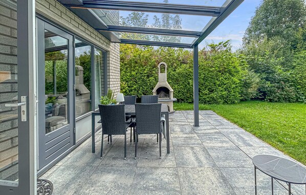 A covered patio with a stone table and chairs, a stone fireplace, and a glass door leading to a room.