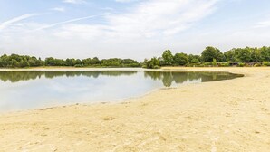 Un lago ampio e tranquillo con una spiaggia sabbiosa e una zona boschiva sullo sfondo.