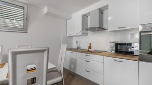 Una cocina moderna con armarios blancos, encimera de madera, microondas integrado y una ventana con persianas.
