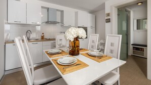 Una cocina moderna con armarios blancos, una isla central con un florero de flores blancas, y una mesa de comedor preparada para cuatro.