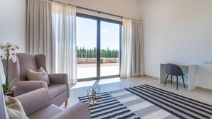Een moderne woonkamer met een bank, een bureau en uitzicht op een aangelegde tuin door grote schuifdeuren.