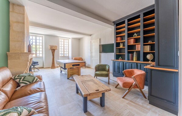 A spacious living room with a leather sofa, a wooden coffee table, a green armchair, and an orange armchair. There is a bookshelf filled with books and decorative items, and a fireplace with a tall, woven floor lamp. - Superbe maison avec piscine (Rauzan)