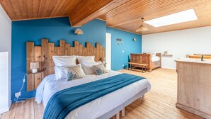 Een slaapkamer met een houten plafond, een bed met een blauwe deken, een houten hoofdbord en een dakraam.
