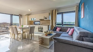 A modern living room with a grey sofa, a dining area with a table and chairs, a kitchen with white cabinets, and large windows offering a view of the city. - Stunning apartment in Medulin with WiFi (Medulin)