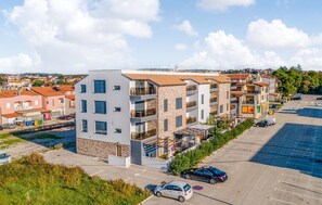 A multi-story residential building with balconies, a parking lot, and a view of a town in the background.