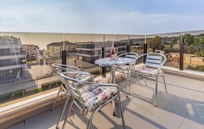 A balcony with a round table and four chairs, overlooking a cityscape with buildings and greenery.
