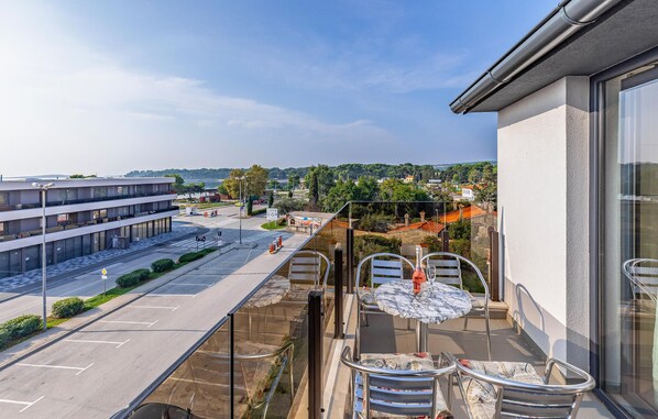 A balcony with a table and chairs, overlooking a parking area and a view of buildings and greenery.