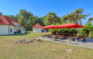 A courtyard with picnic tables and red umbrellas, surrounded by buildings with red roofs and a grassy area. - Pet friendly apartment in Altenkirchen with house a panoramic view (Altenkirchen)