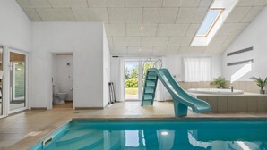A modern indoor pool area with a slide, a jacuzzi, and a view of the outdoors. - Pet friendly home in Idestrup with sauna (Idestrup)