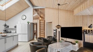 A modern kitchen with white appliances, a dining area with leather chairs, a flat-screen TV, and a wooden interior. - Pet friendly home in Idestrup with sauna (Idestrup)