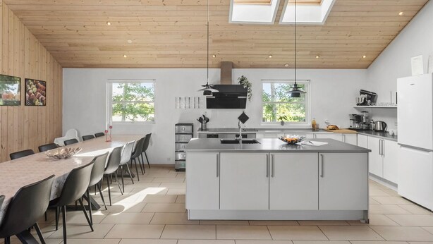A modern kitchen with a central island, white cabinetry, and a dining area with a table and chairs. - Pet friendly home in Idestrup with sauna (Idestrup)