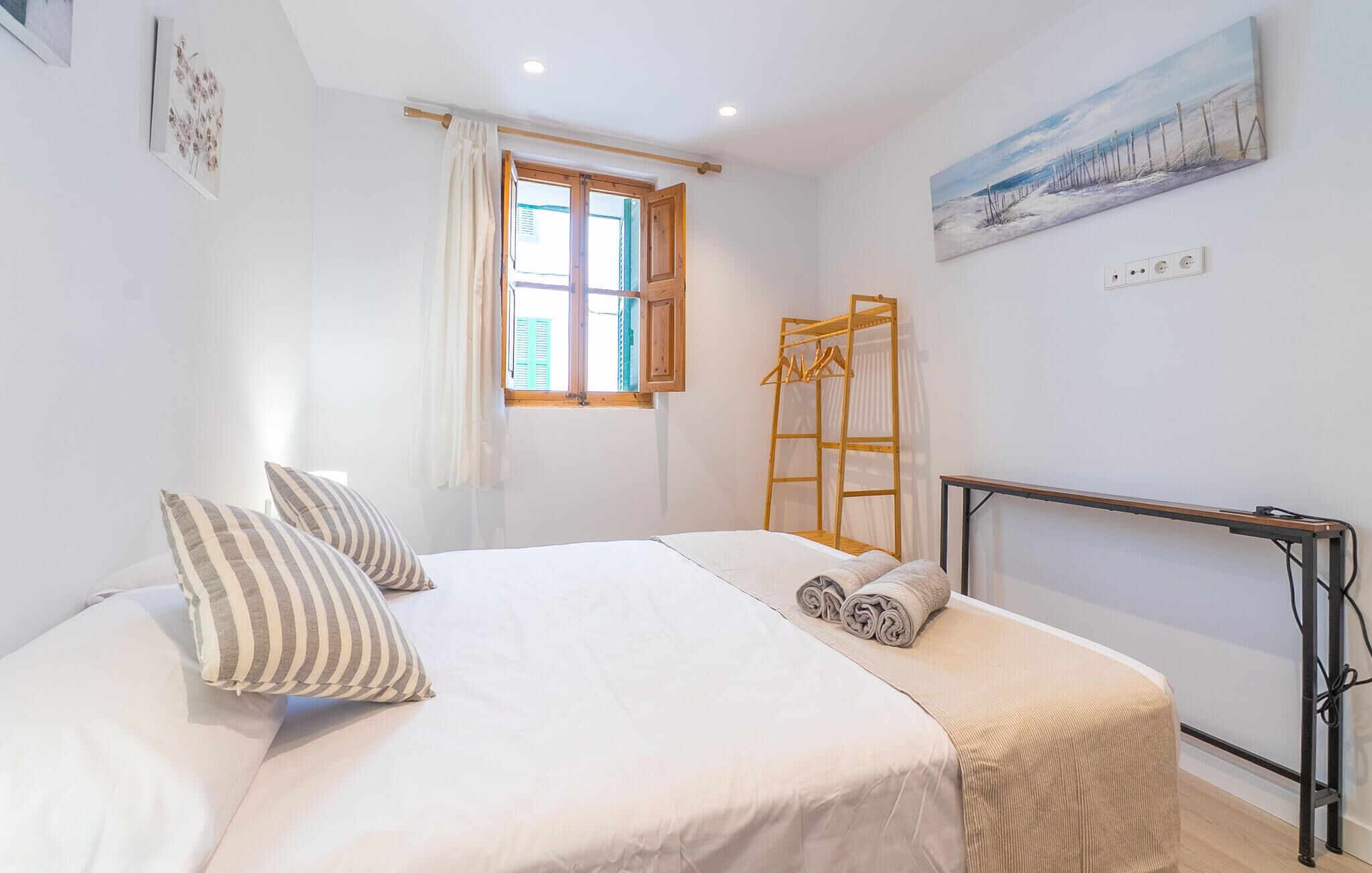 A bedroom with a bed, pillows, a wooden ladder, a window, and a painting on the wall.