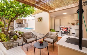 Un patio exterior con piscina, dos sillas acolchadas, una pequeña mesa redonda con fruta y una mesa de fútbol de mesa.
