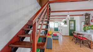 A wooden staircase leading to a living area with a dining table and chairs, a green door, and a clock on the wall.