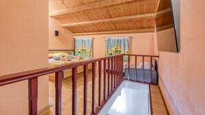 A hotel room with a wooden ceiling, a balcony with a wooden railing, and two beds with sunflowers on the windowsills.