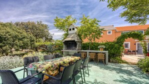 An outdoor patio with a dining table and chairs, a barbecue grill, and a building in the background.