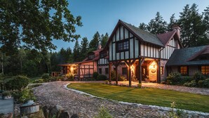 Una casa de estilo Tudor con entrada de piedra, césped cuidado y un fondo de bosque.
