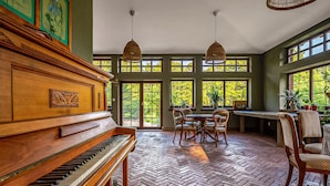 Amplia habitación con un piano de cola, una mesa de comedor con sillas y grandes ventanas con vistas a zonas verdes.