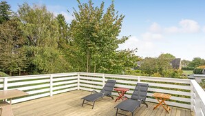 A wooden deck with white railings, two lounge chairs, a small table, and a red folding table.