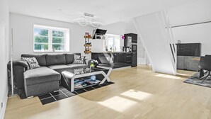 A modern living room with a grey sofa, a coffee table, and a kitchen area with black cabinets and a white countertop.
