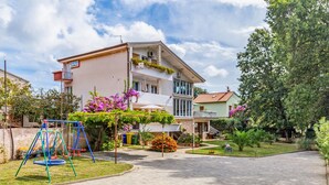 A two-story building with a balcony and a garden area with flowers and a swing set.