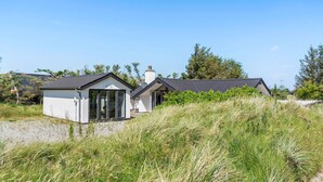 A coastal house with a large glass door, a chimney, and a grassy foreground. - Amazing home in Thisted with sauna (Thisted)