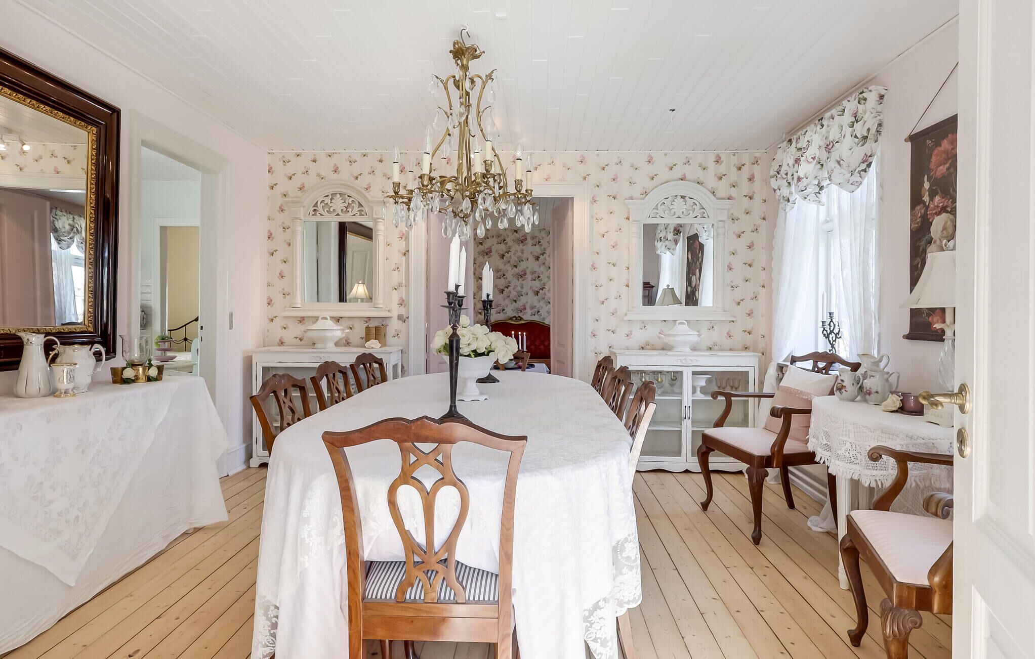 Une salle à manger avec une table ronde, des chaises, un lustre et un papier peint à motifs floraux.