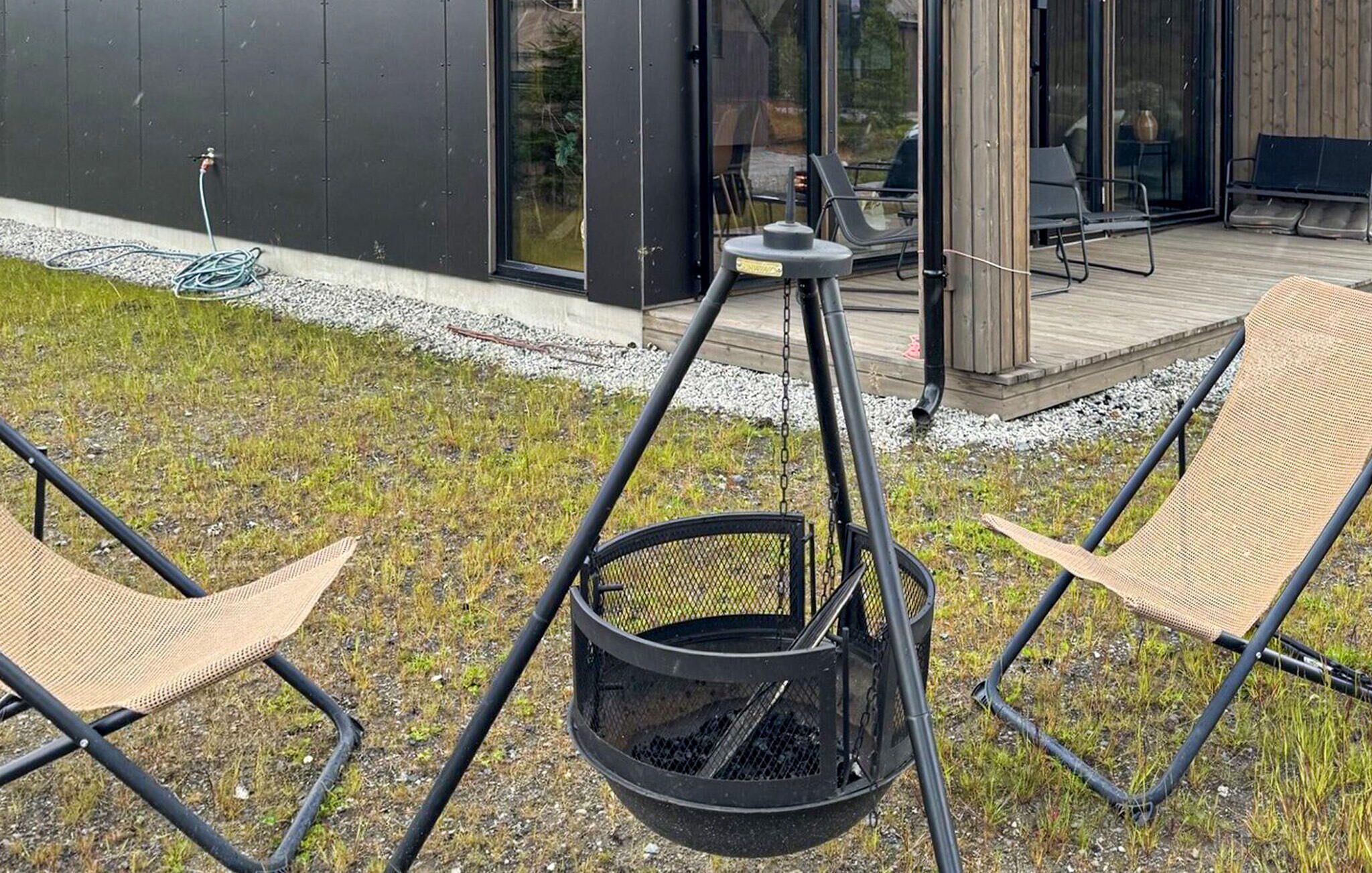 Zona salotto esterna moderna con due poltrone in vimini e un braciere sospeso.