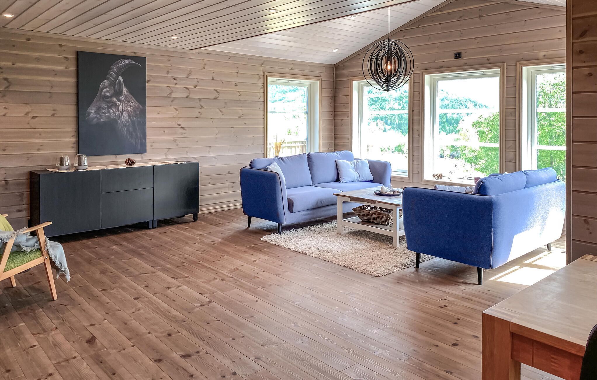 A modern living room with a blue sofa set, a dark grey cabinet, and a wooden ceiling.