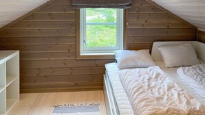 Een kleine kamer met schuin dak, een enkel bed, een raam en een witte bergkast.