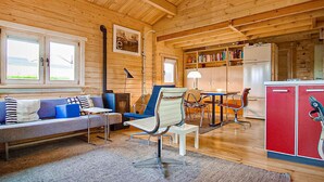 A cozy cabin interior with a wooden ceiling, a sofa, a dining table, and a kitchen area.