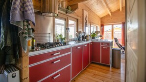 A kitchen with red cabinets, a sink, and a stove. There is a window and a door leading outside.