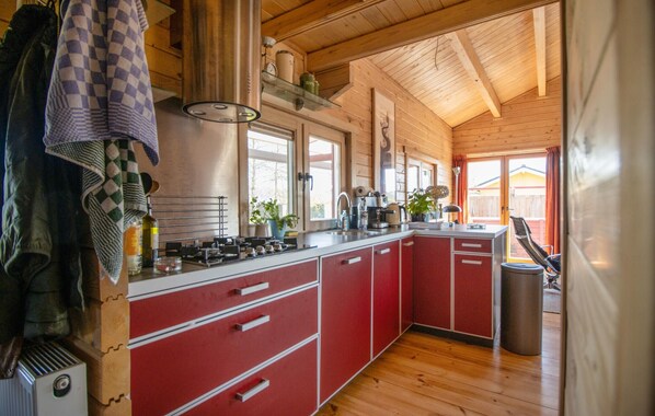 A kitchen with red cabinets, a sink, and a stove. There is a window and a door leading outside.