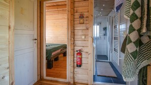 A wooden cabin interior with a bed, a fire extinguisher, and a hallway leading to a bathroom.