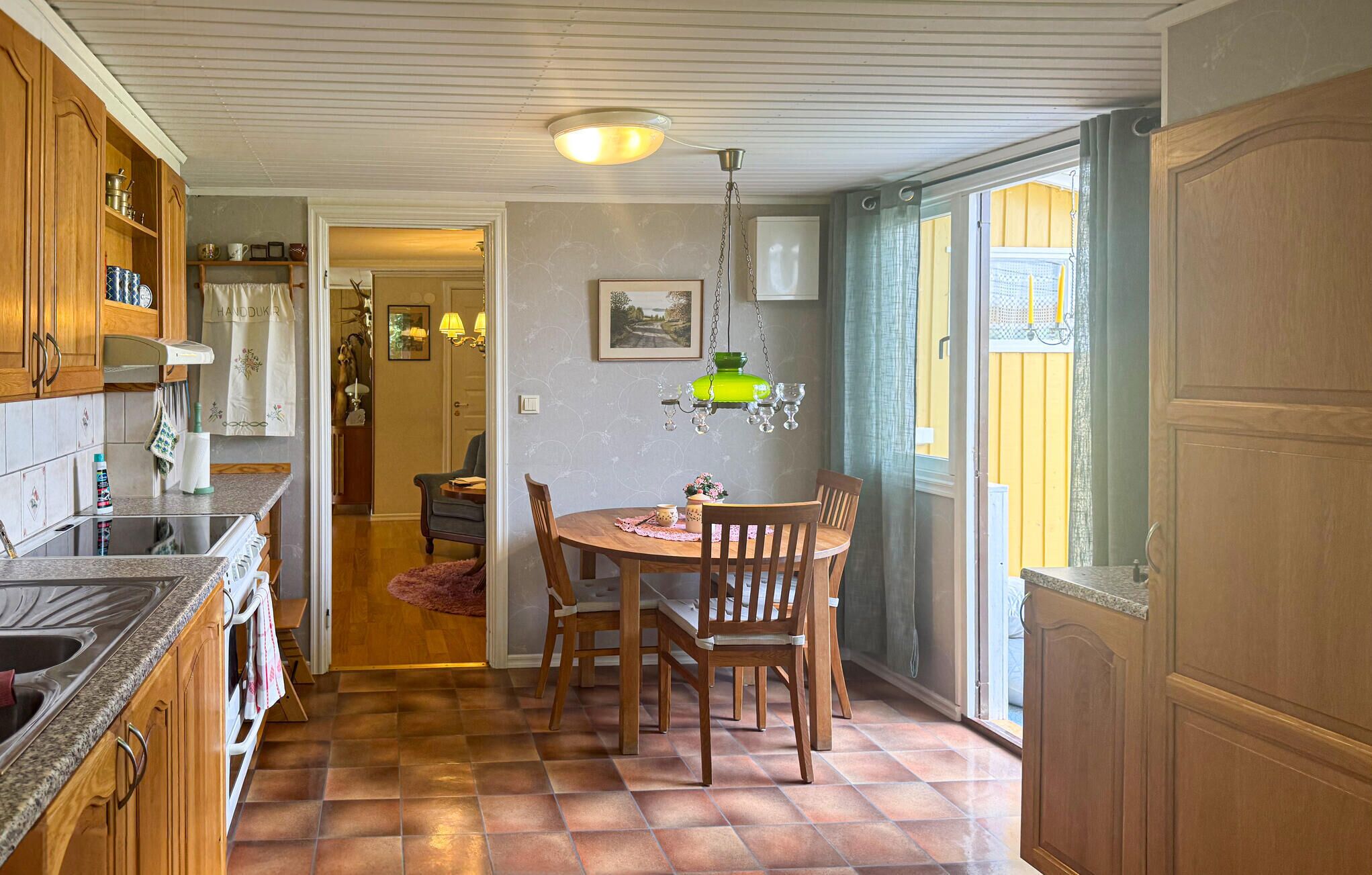Une cuisine avec des meubles en bois, une table à manger avec des chaises, un luminaire suspendu et une vue par la fenêtre.