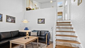 Een moderne woonkamer met een zwarte leren bank, een houten salontafel en een trap met houten treden.