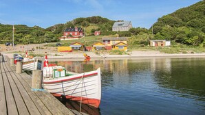 Een houten steiger met aanliggende boten, een zandstrand en kleurrijke huizen op de achtergrond.