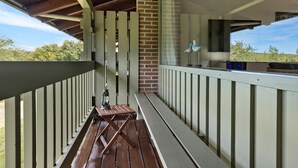 Een overdekt terras buiten met een houten tafel en bankjes, een lantaarn en een bakstenen muur.