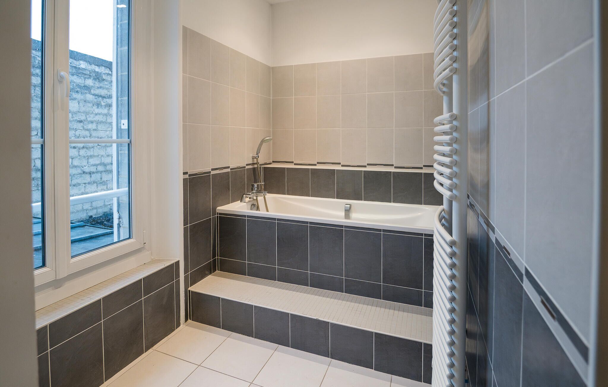 A modern bathroom with a bathtub, a window, and a radiator.