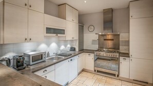 A modern kitchen with white cabinetry, a built-in oven, a microwave, and a coffee maker. - Charmante maison de ville (Chantilly)