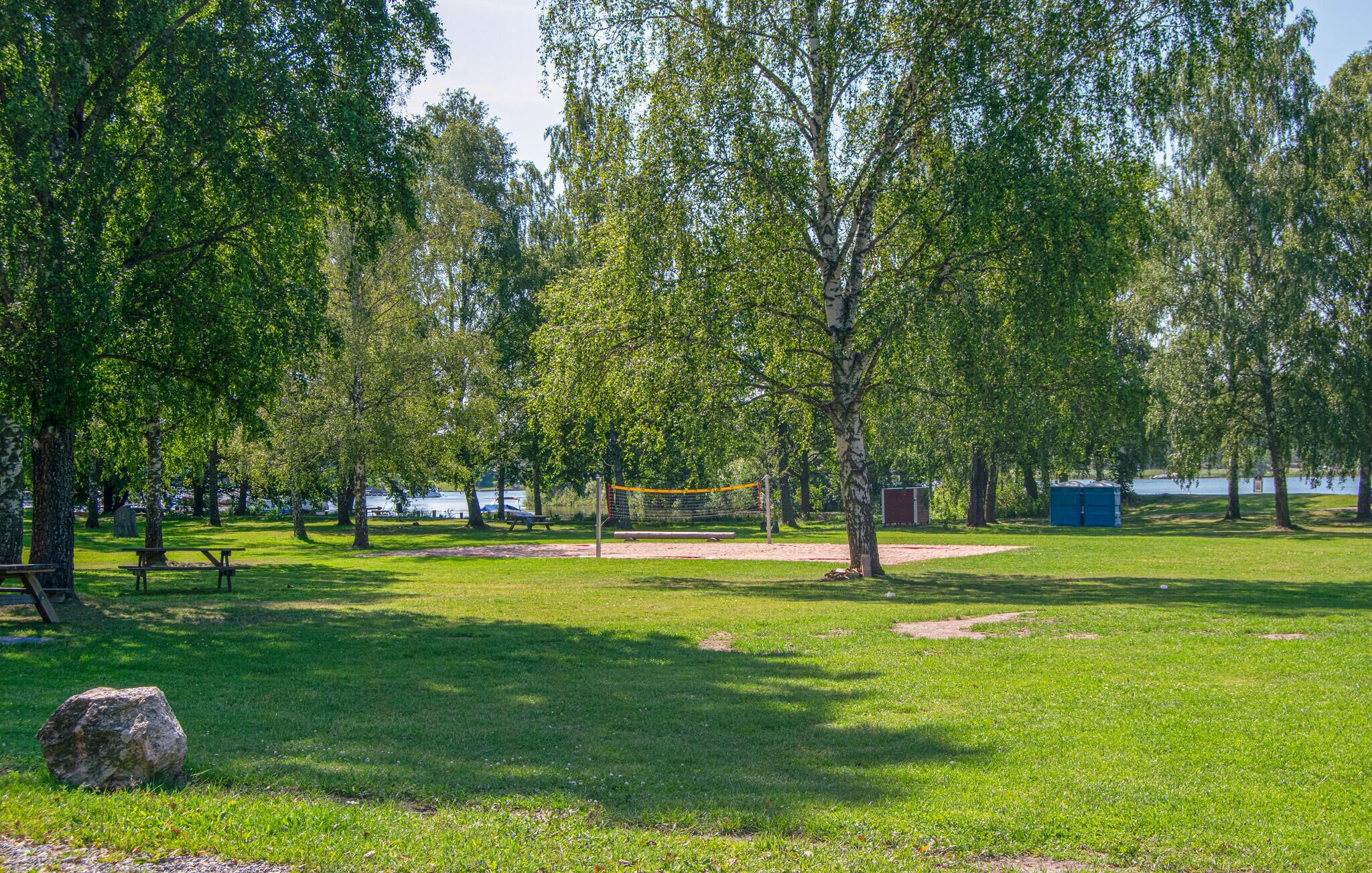 Un parque con una red de voleibol, mesas de picnic y un cobertizo pequeño.