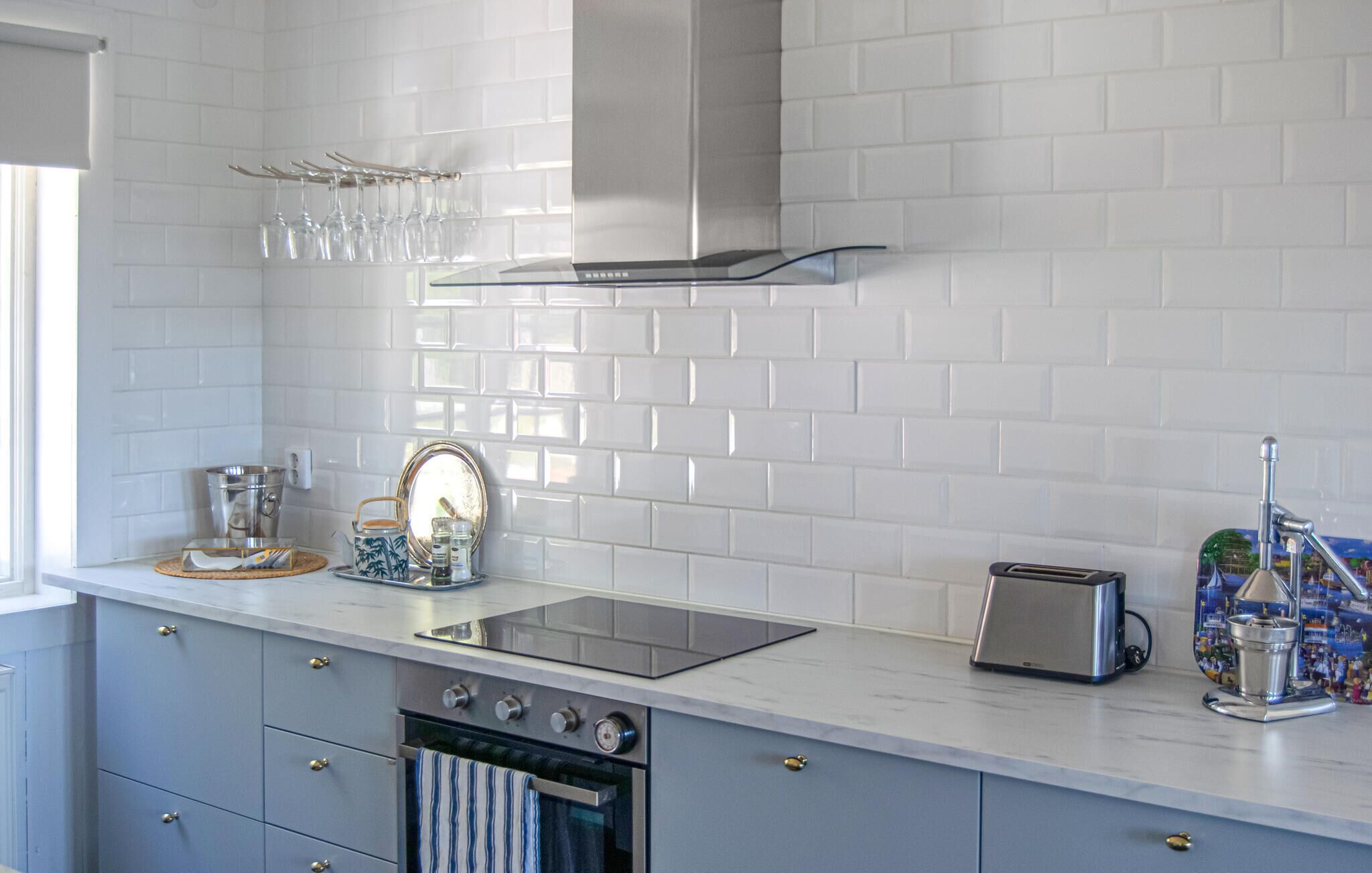 A modern kitchen with white subway tiles, a stainless steel range hood, a built-in oven, a toaster, and a kettle on the countertop.