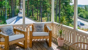 A wooden deck with two chairs and a table, surrounded by a white railing, overlooking a forested area.