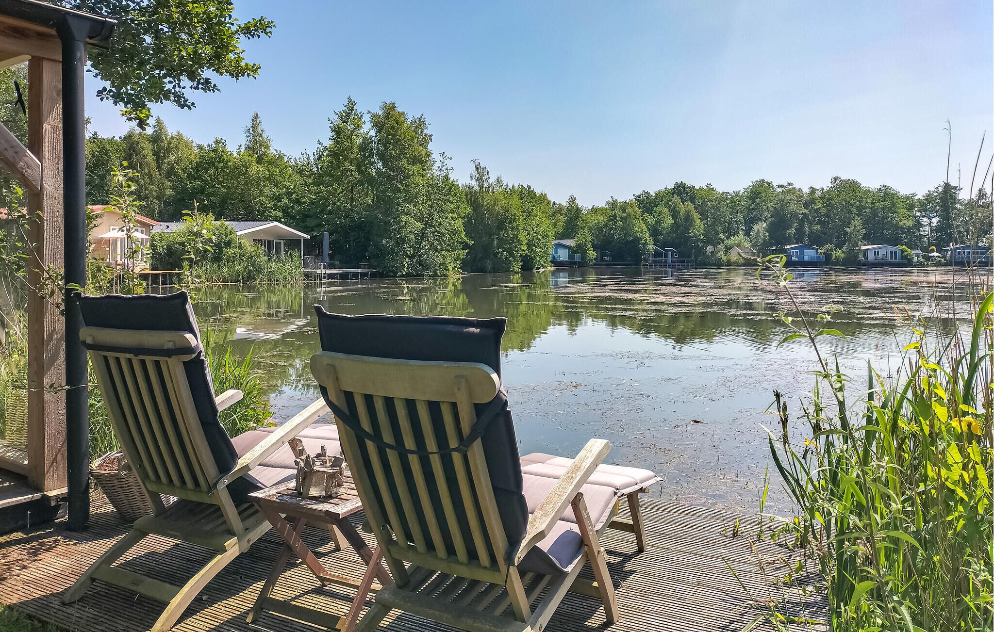 Dos sillones de descanso en una terraza de madera con vistas a un lago y casas al fondo.