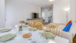 A dining area with a table set for four, a television in the background, and a kitchenette visible through an open door.