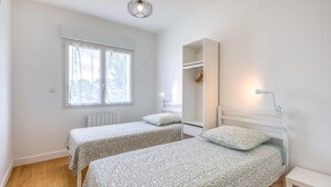 A room with two beds, a window, a radiator, a hanging light fixture, and a white wardrobe.
