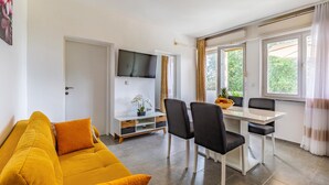 A modern living room with a yellow sofa, a dining area with a white table and chairs, a flat-screen TV mounted on the wall, and large windows with curtains. - Lovely apartment in Banjole with WiFi (Banjole)