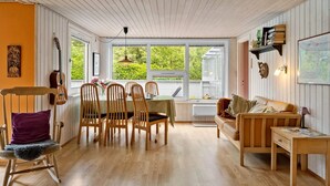 A cozy room with a dining table, chairs, a sofa, and a window with a view of greenery.