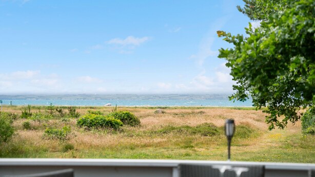 A view from a restaurant with a table and chairs, overlooking a grassy area and the ocean.